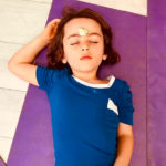 pre-schooler with small stone on forehead in yoga resting pose