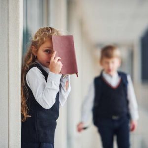 anxious school girl hiding behind book